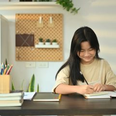 Focused teenage girl doing homework at home, writing down in notebook. Learning and education concept.